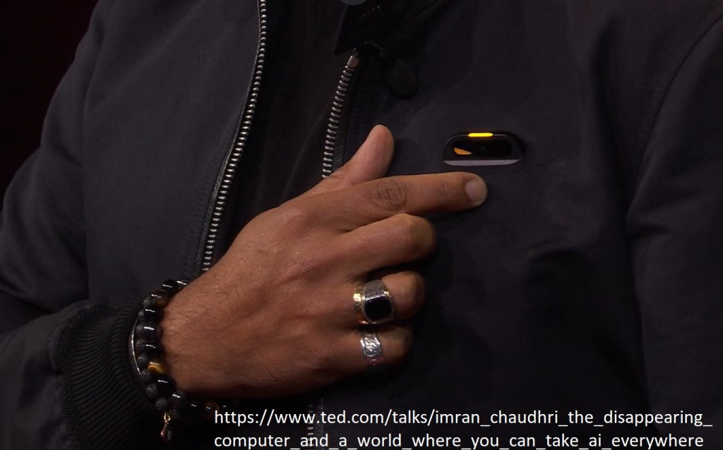 Imran Choudry pointing at wearable AI extension clip.
Imran Choudry wskazuje palcem klip na ubraniu podłączony do sztucznej inteligencji.